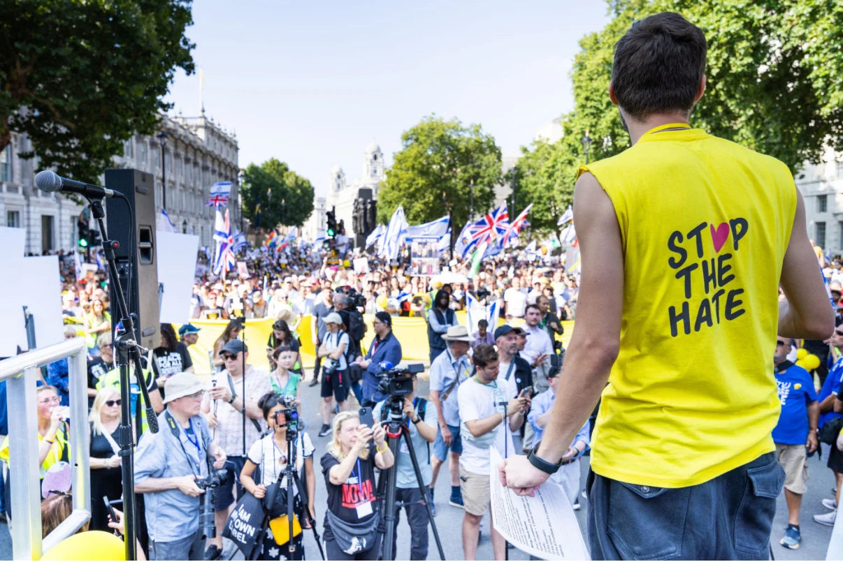 A person in a yellow Stop The Hate shirt faces a crowd on a London street.