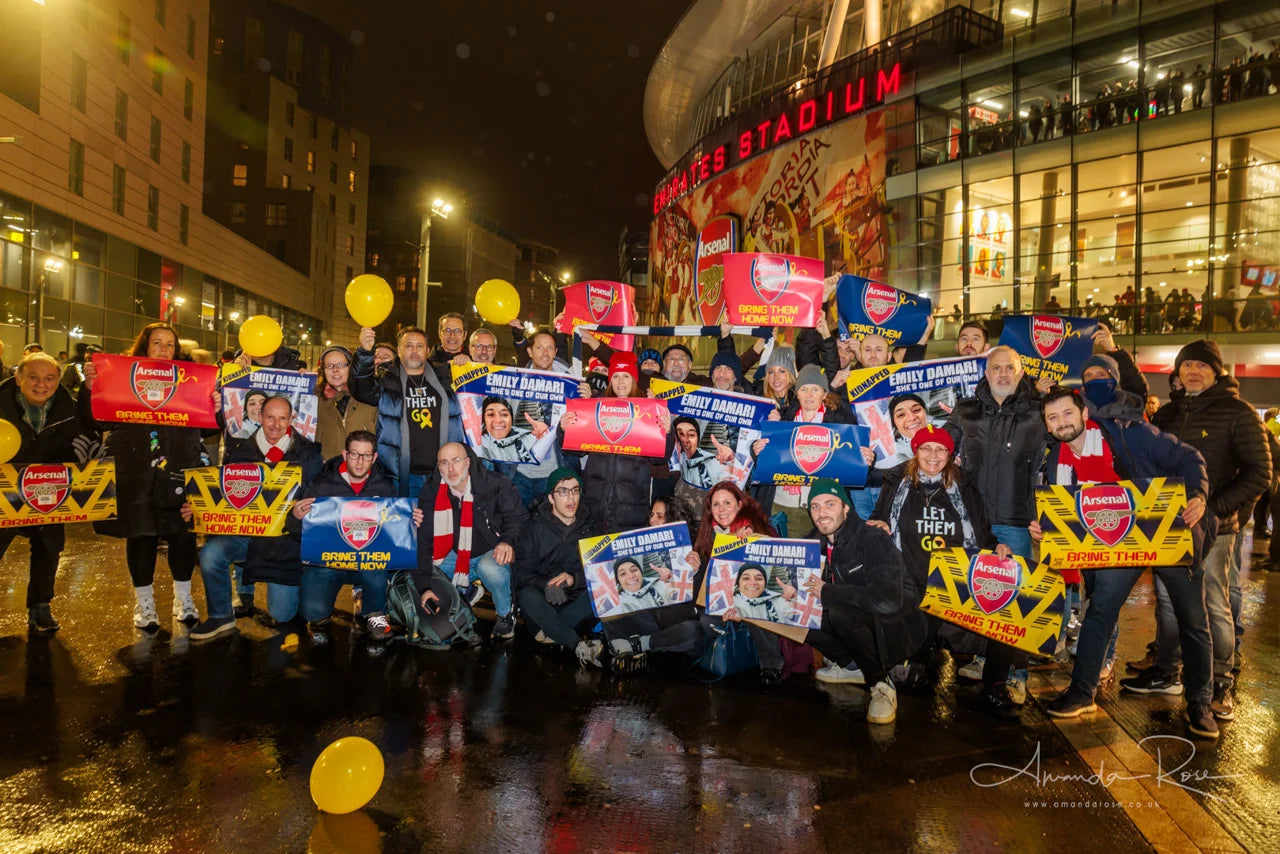 People outside the Emirates Stadium hold football banners and photographs of hostages.