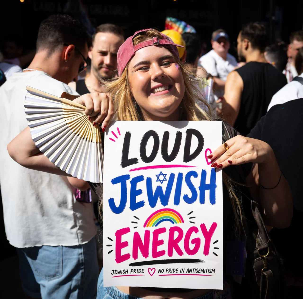 A smiling participant holds a handmade Loud Jewish Energy sign.